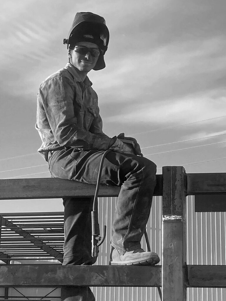 Anthony Segura (owner of Segura Steel welding services in Phoenix area) wearing a welding helmet while sitting on a fence